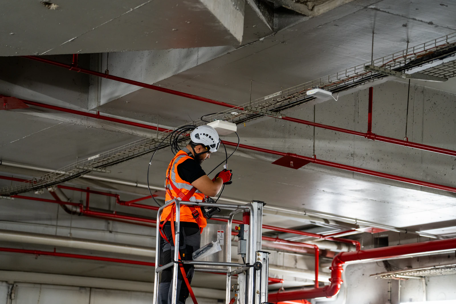Technician on a lift installing life-safety devices in an exposed industrial ceiling