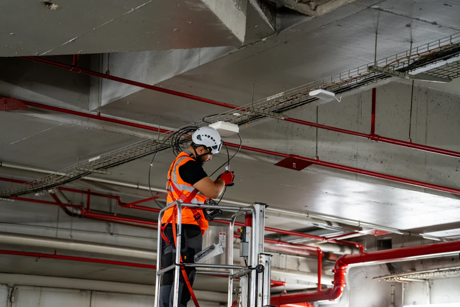 Technician on a lift installing ceiling components among red sprinkler pipes