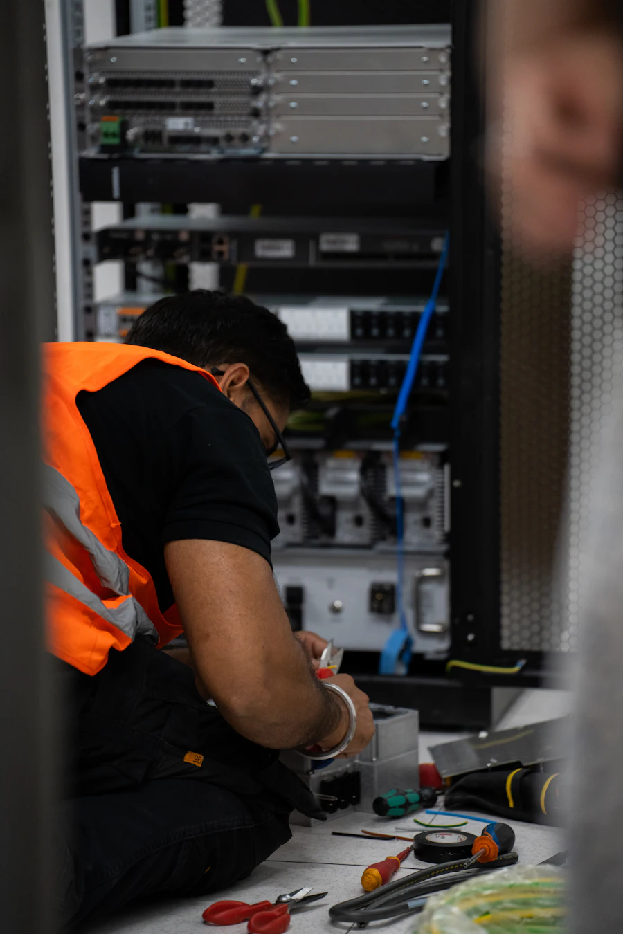 Technician in a high-visibility vest servicing rack equipment with hand tools