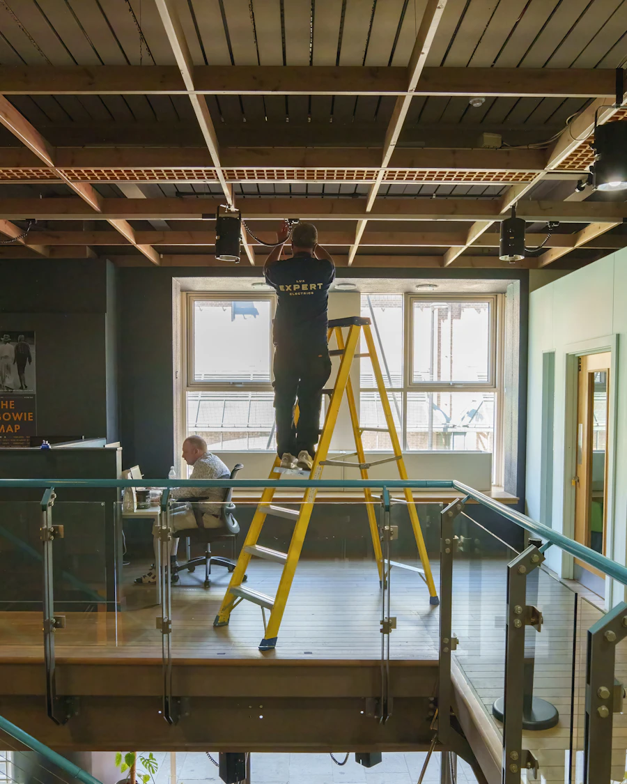 Technician on a yellow ladder installing ceiling equipment in an office